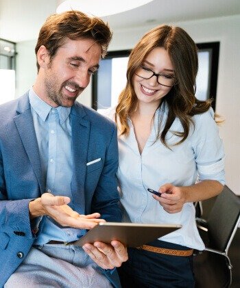 A man and woman in business attire focused on a tablet, discussing work-related matters.